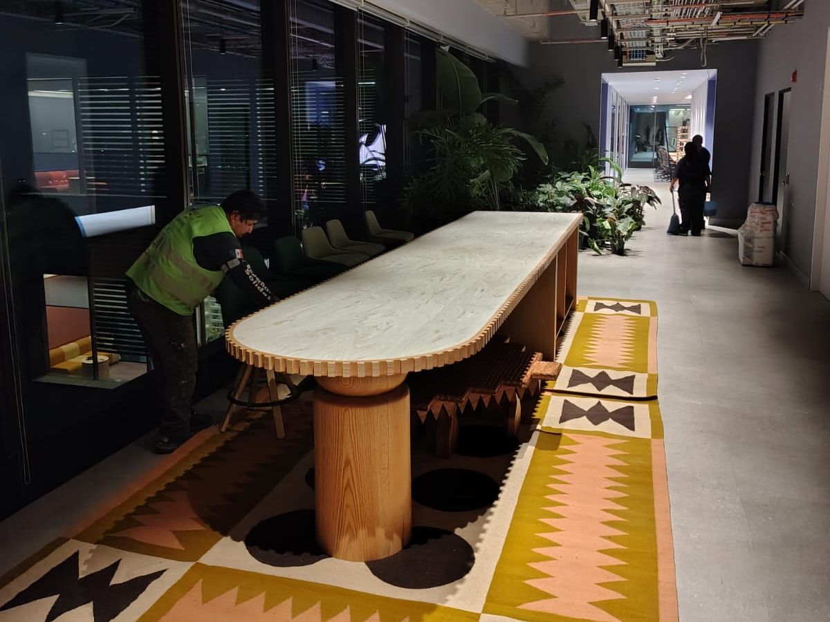 Mesa larga ovalada de cubierta clara con canto acanalado y base de madera en un pasillo