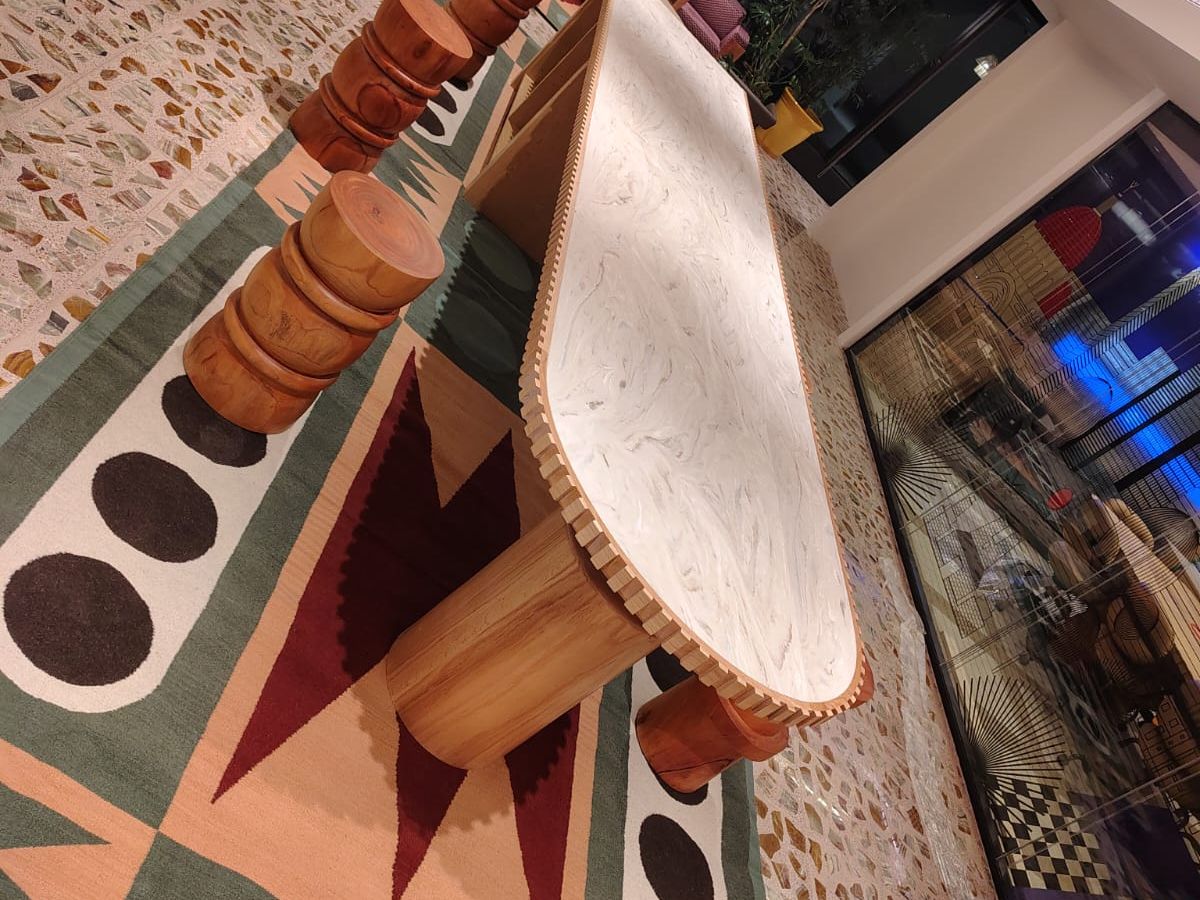 Mesa ovalada de cubierta clara con canto acanalado y base de madera sobre un tapete de colores